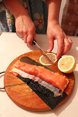 Image showing hand cuts slices of a red fish and lemon