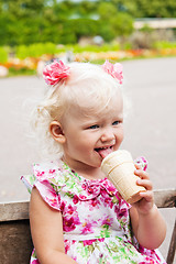 Image showing The small blond girl eats ice-cream in a summer garden