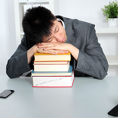 Image showing Asian man sleeping on top of a pile of books