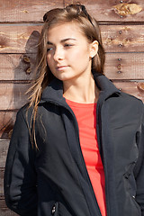 Image showing portrait of a young girl standing against a wooden wall