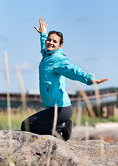 Image showing Beautiful girl in a jacket kneeling on a rock