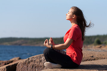 Image showing Young girl in lotus pose on the rocks