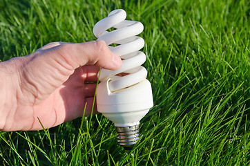 Image showing energy saving lamp in hand over green grass