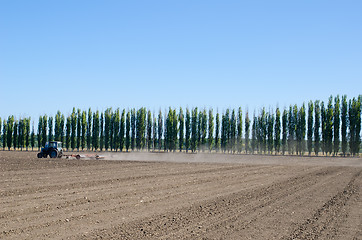 Image showing agriculture tractor on black ploughed field under blue sky