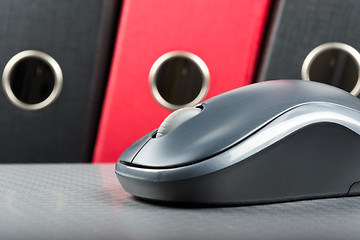 Image showing A wireless mouse placed on notebook and three folders in the bac