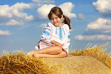 Image showing small rural girl on the straw after harvest field with straw bal