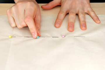 Image showing Closeup of large upholstery pins being pinned into plain fabric