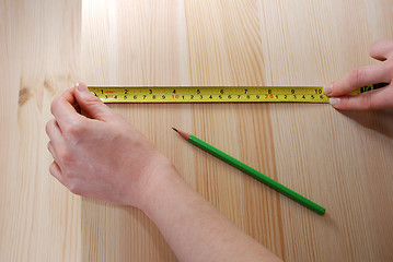 Image showing Two hands measure a wooden board with a steel tape measure