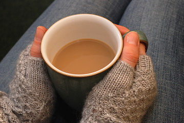 Image showing A woman in a cosy jumper holds a cup of tea or coffee on her lap