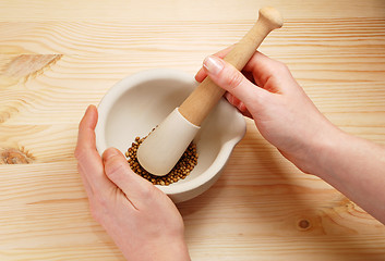 Image showing Two hands holding a pestle and mortar with whole coriander seeds