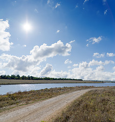 Image showing sun on cloudy sky over rural road and river near it