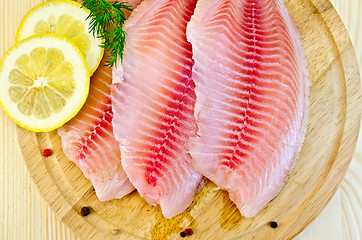 Image showing Fillets tilapia with lemon on a round board