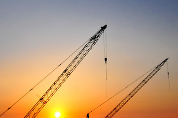 Image showing Industrial construction cranes and building silhouettes over sun