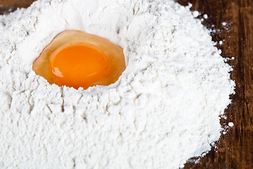 Image showing broken egg on flour on wooden table