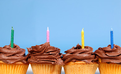 Image showing Four chocolate frosted cupcakes in a row with candles