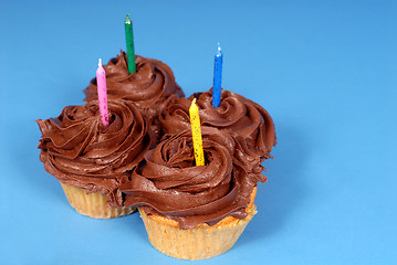 Image showing Four chocolate frosted cupcakes with candles with a blue backgro