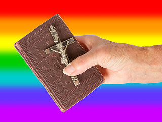 Image showing Old hand (woman) holding a very old bible, rainbow flag