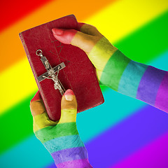 Image showing Old hands holding a very old bible, rainbow flag pattern