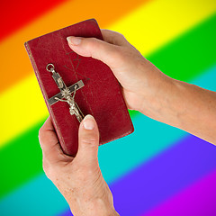 Image showing Old hands holding a very old bible, rainbow flag pattern