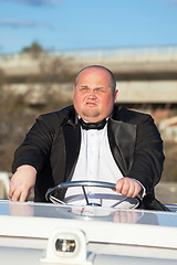 Image showing Overweight man in a tuxedo at the helm of a pleasure boat