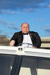 Image showing Overweight man in a tuxedo at the helm of a pleasure boat