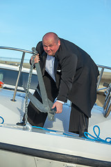Image showing Fat man in tuxedo lifting an anchor