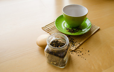 Image showing herbs in glass jar and spilled tea near cup on wooden tray 