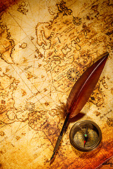 Image showing Vintage compass and goose quill pen lying on an old map.