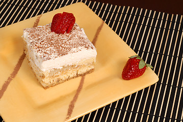 Image showing A piece of tiramisu dusted with cocoa on a yellow plate with two