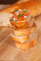 Image showing Stack of bruschetta on a cutting board with loaf of bread in bac