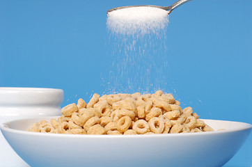 Image showing Spoon sprinkling sugar on a bowl of oat cereal on blue backgroun