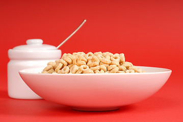 Image showing Bowl of oat cereal with sugar bowl on red background