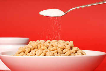 Image showing A spoon sprinkling sugar on a bowl of oat cereal on red backgrou