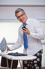 Image showing Businessman text messaging while ironing pants