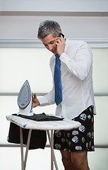 Image showing Talking on a mobile phone while ironing pants