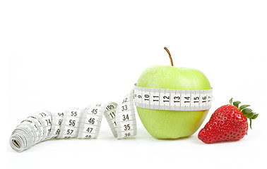 Image showing Measuring tape wrapped around a green apple and strawberry as a symbol of diet
