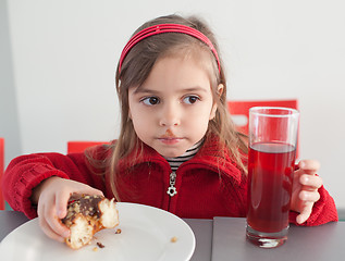 Image showing Little girl eating donut with juice