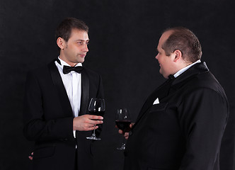 Image showing Two stylish businessman in tuxedos with glasses of red wine