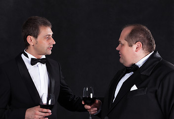 Image showing Two stylish businessman in tuxedos with glasses of red wine