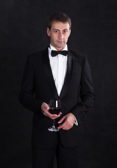 Image showing Stylish man in elegant black tuxedo with glass red wine