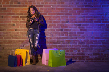 Image showing Woman with Shopping Bags Using Cell Phone Against Brick Wall