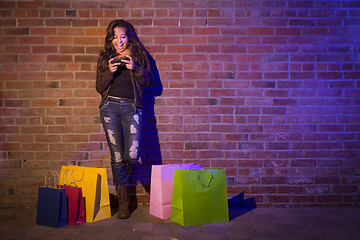 Image showing Woman with Shopping Bags Using Cell Phone Against Brick Wall