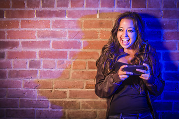 Image showing Mixed Race Woman Using Her Cell Phone Against Brick Wall