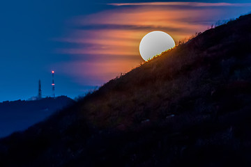 Image showing Moon shining bright behind black mountains