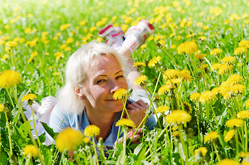 Image showing A woman lies in a clearing and sniffs a flower  