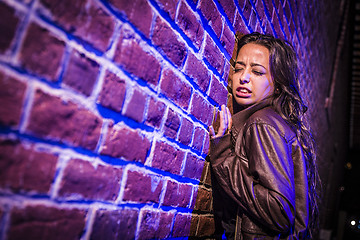 Image showing Frightened Pretty Young Woman Against Brick Wall at Night