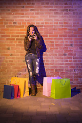 Image showing Woman with Shopping Bags Using Cell Phone Against Brick Wall