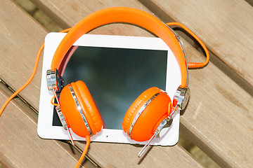 Image showing White tablet PC with orange headphones on the wood bench