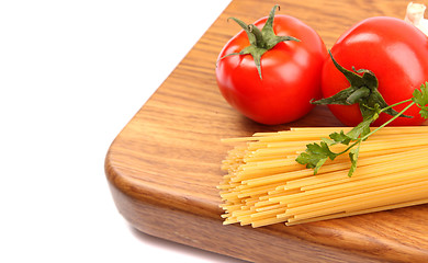 Image showing uncooked spaghetti, garlic and tomatos on a preparation board are located left