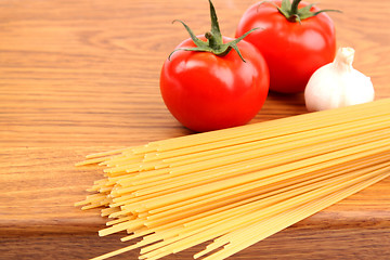 Image showing uncooked spaghetti, garlic and tomatos on a preparation board